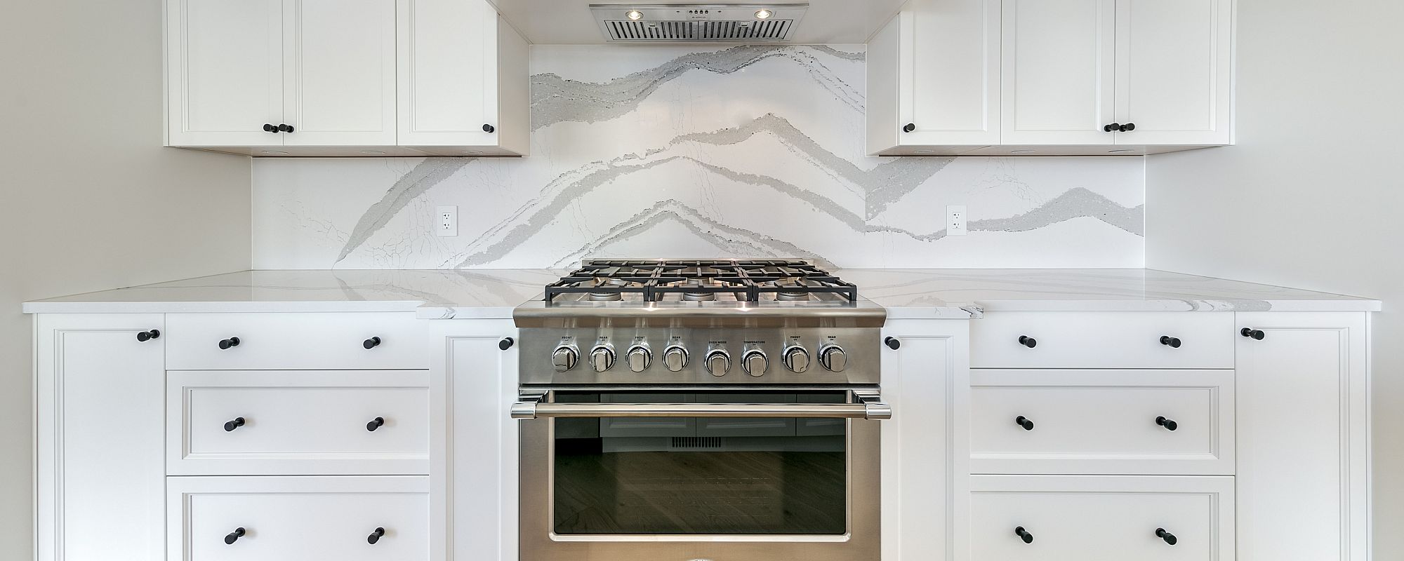 Closeup of a Stark Homes kitchen stove area with marble style backsplash and crisp white cabinets