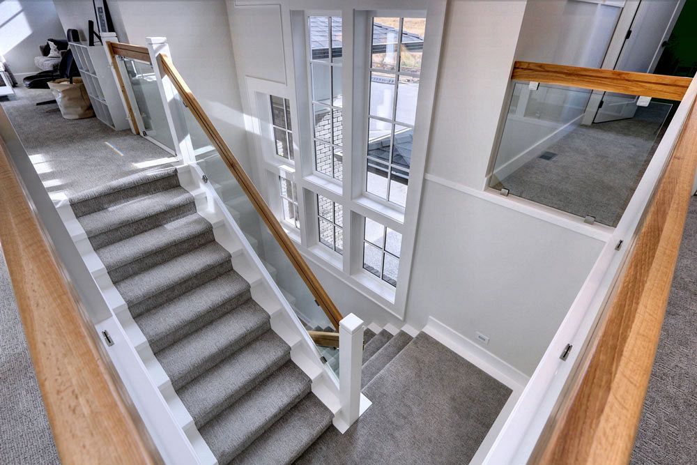 Custom home build view down from platform in open concept home, overlooking wooden railing and carpeted stairs with large windows