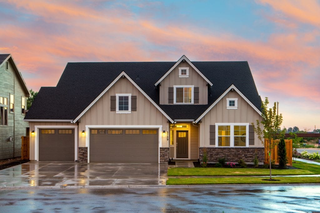 Modern farmhouse home light brown exterior, med brown garage doors, and black roof.