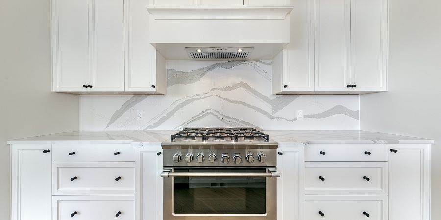 Marble design backsplash in custom kitchen with large gas stovetop and white cabinets